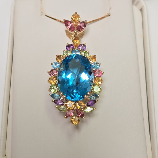 14K gold oval blue topaz pendant from Chique Jewelry showcasing a sparkling blue gemstone on a gold chain.