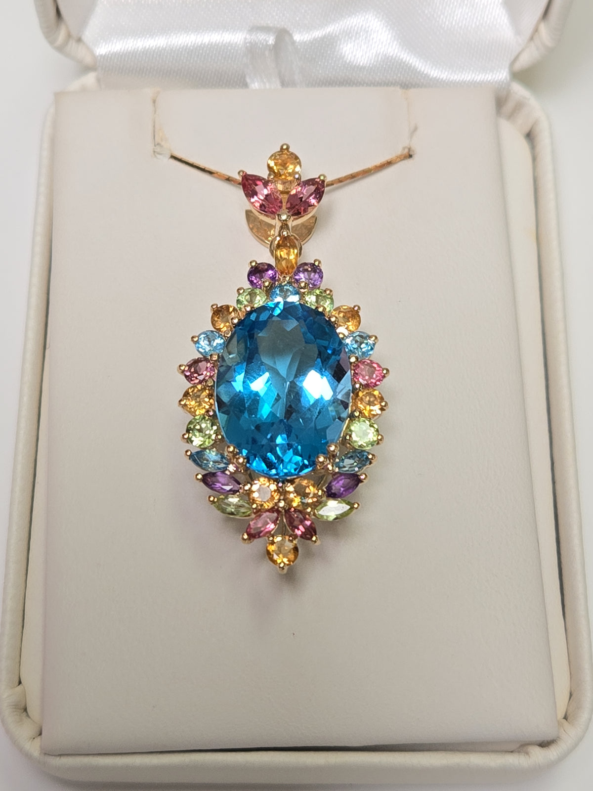 14K gold oval blue topaz pendant from Chique Jewelry showcasing a sparkling blue gemstone on a gold chain.
