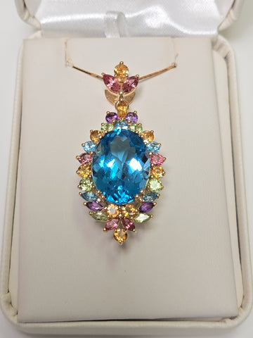 14K gold oval blue topaz pendant from Chique Jewelry showcasing a sparkling blue gemstone on a gold chain.