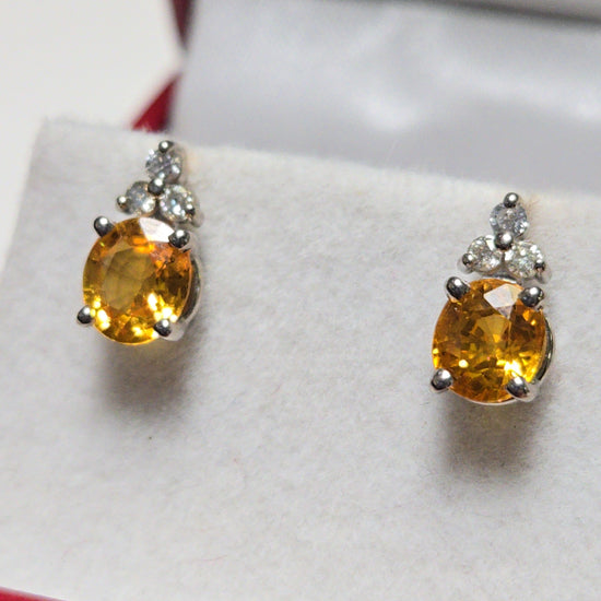 14K white gold stud earrings with 1.6ct oval orange sapphire, featuring elegant design and sparkling gemstone detail.