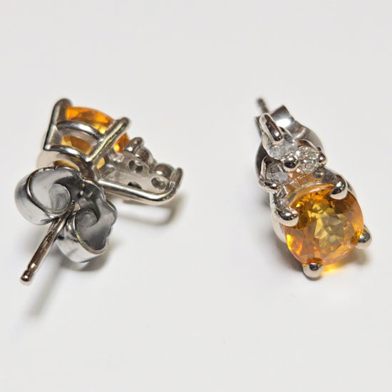 14K white gold stud earrings with 1.6ct oval orange sapphire, featuring elegant jewelry design and sparkling gemstone accents.