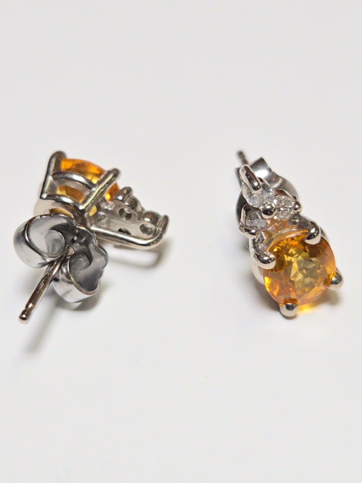 14K white gold stud earrings with 1.6ct oval orange sapphire, featuring elegant jewelry design and sparkling gemstone accents.